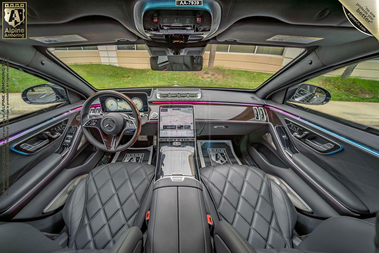 Interior view of a luxurious Mercedes-Benz Maybach, featuring a panoramic sunroof, diamond-stitched leather seats, a large touchscreen display, and ambient lighting. The car dashboard showcases a high-tech design.