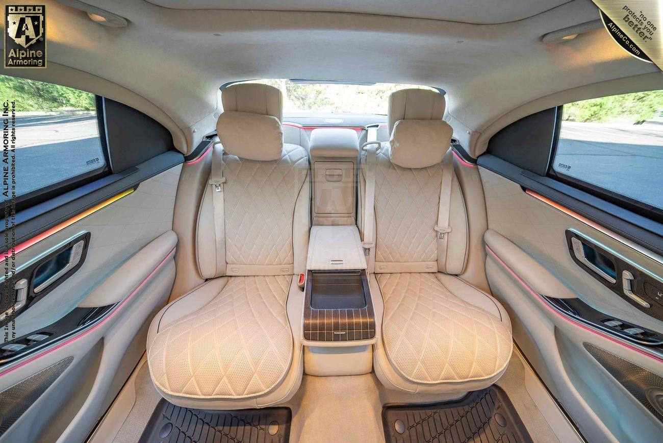 Interior of an armored Mercedes-Benz S580 sedan with beige leather seats, a center console, and wooden panel accents.