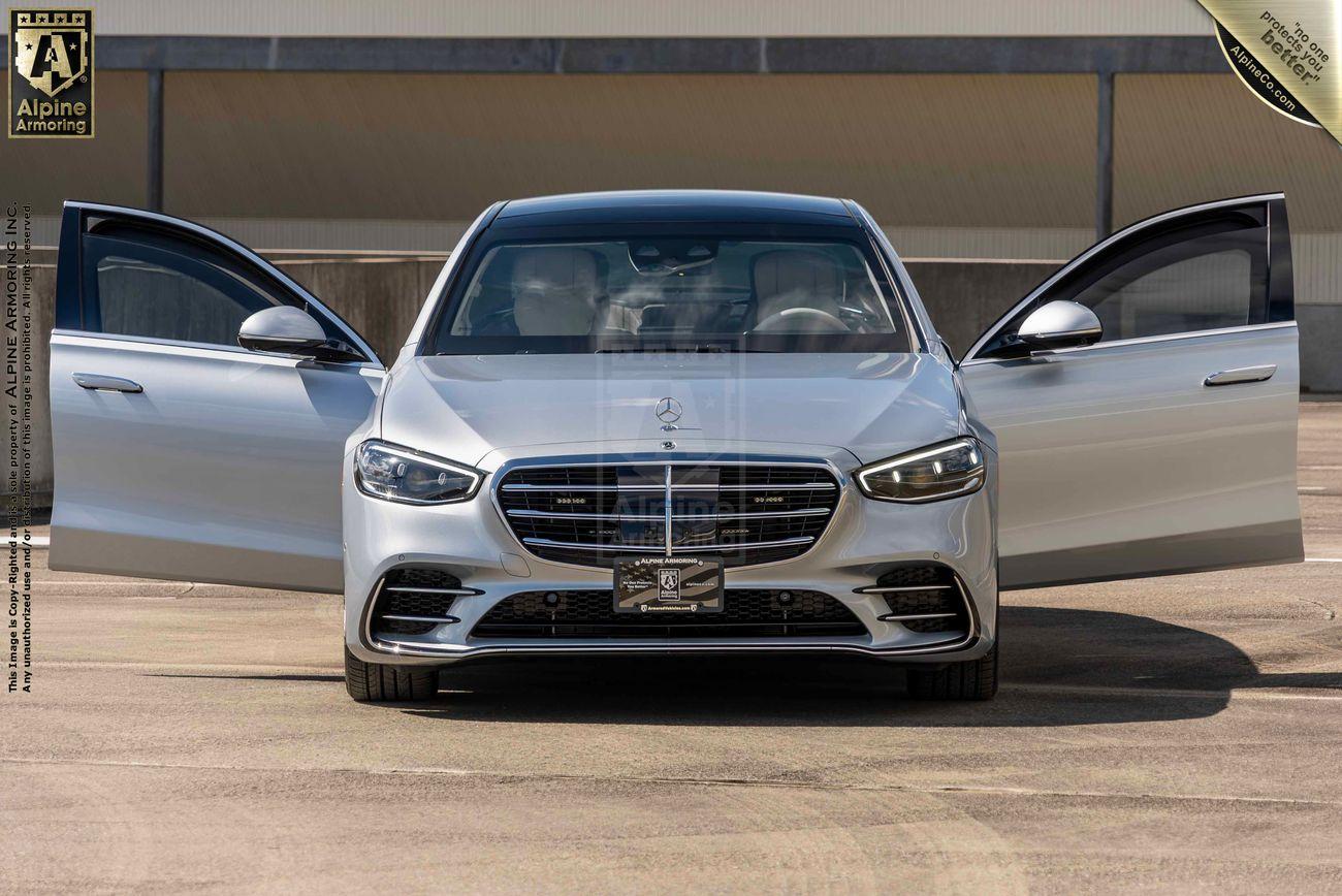 A silver armored silver Mercedes-Benz S580 sedan with both front doors open, displayed in an outdoor setting.