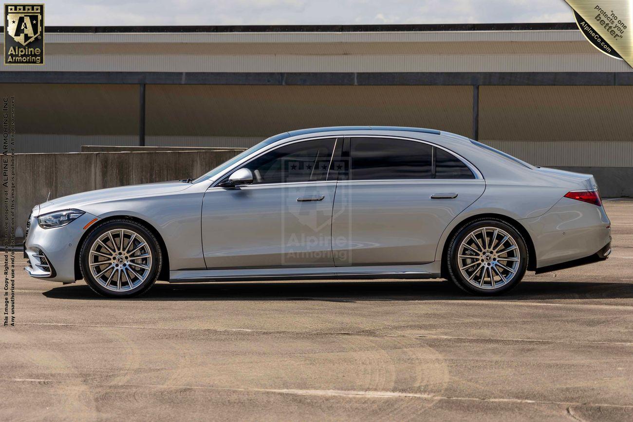 An armored silver Mercedes-Benz S580 sedan parked outdoors, showcasing its side profile against a building backdrop.