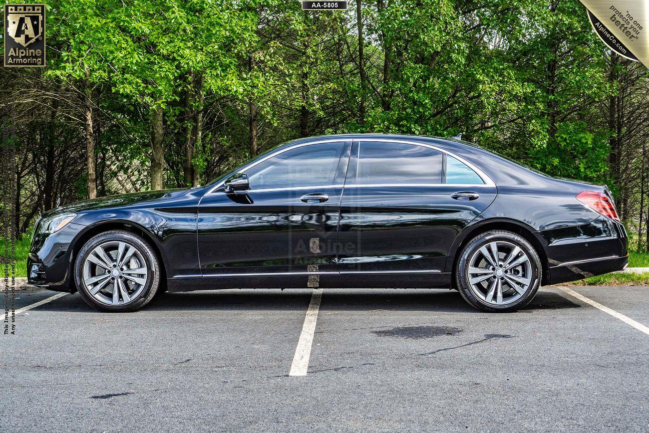 Side view of a black Mercedes-Benz 560 sedan parked in an outdoor lot with a background of green trees.