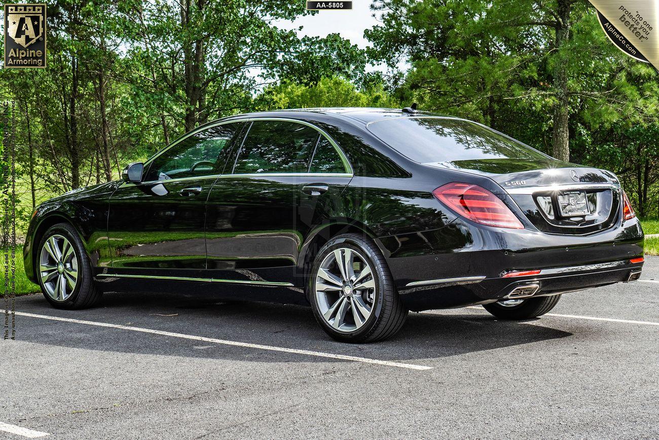 A black luxury Mercedes-Benz S560 sedan is parked in an outdoor setting, surrounded by greenery. The car is positioned at a slight angle, showcasing its rear and left side.