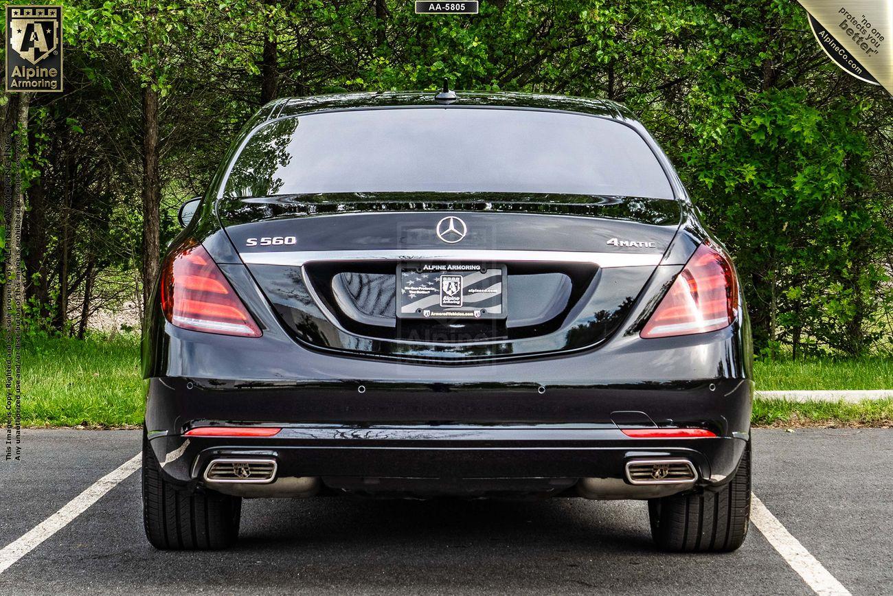 A black Mercedes-Benz S560 sedan is parked on a paved surface with trees in the background. The car's license plate is from 'Alpine Armoring'.