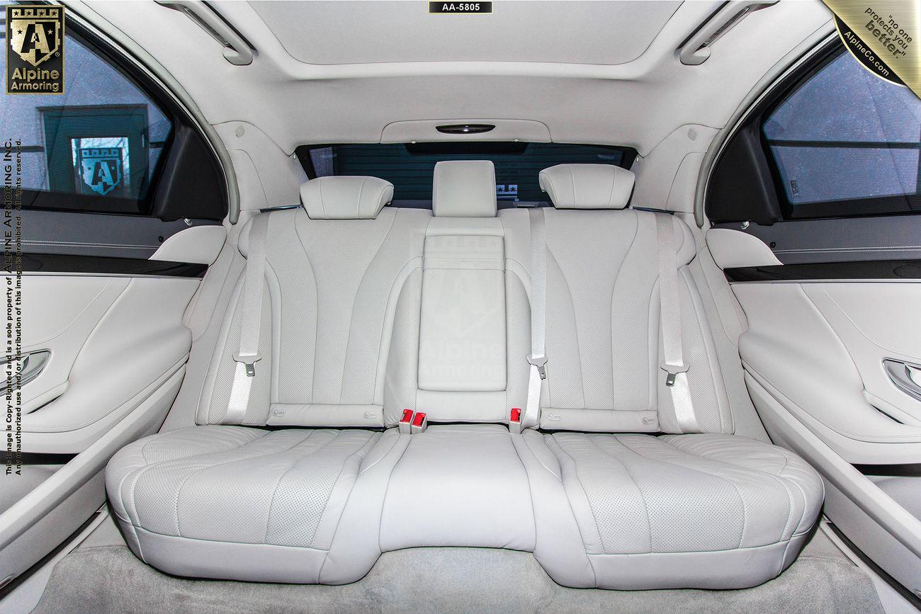 A spacious luxury Mercedes-Benz 560's rear seat featuring light grey leather upholstery, seat belts, and headrests. The interior is clean and includes a center armrest. The car's doors have metallic trim accents.