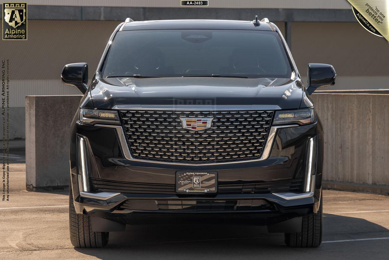 Front view of a black, armored Cadillac Escalade ESV Premium Luxury SUV parked in a concrete area, featuring a prominent grille and modern headlight design.