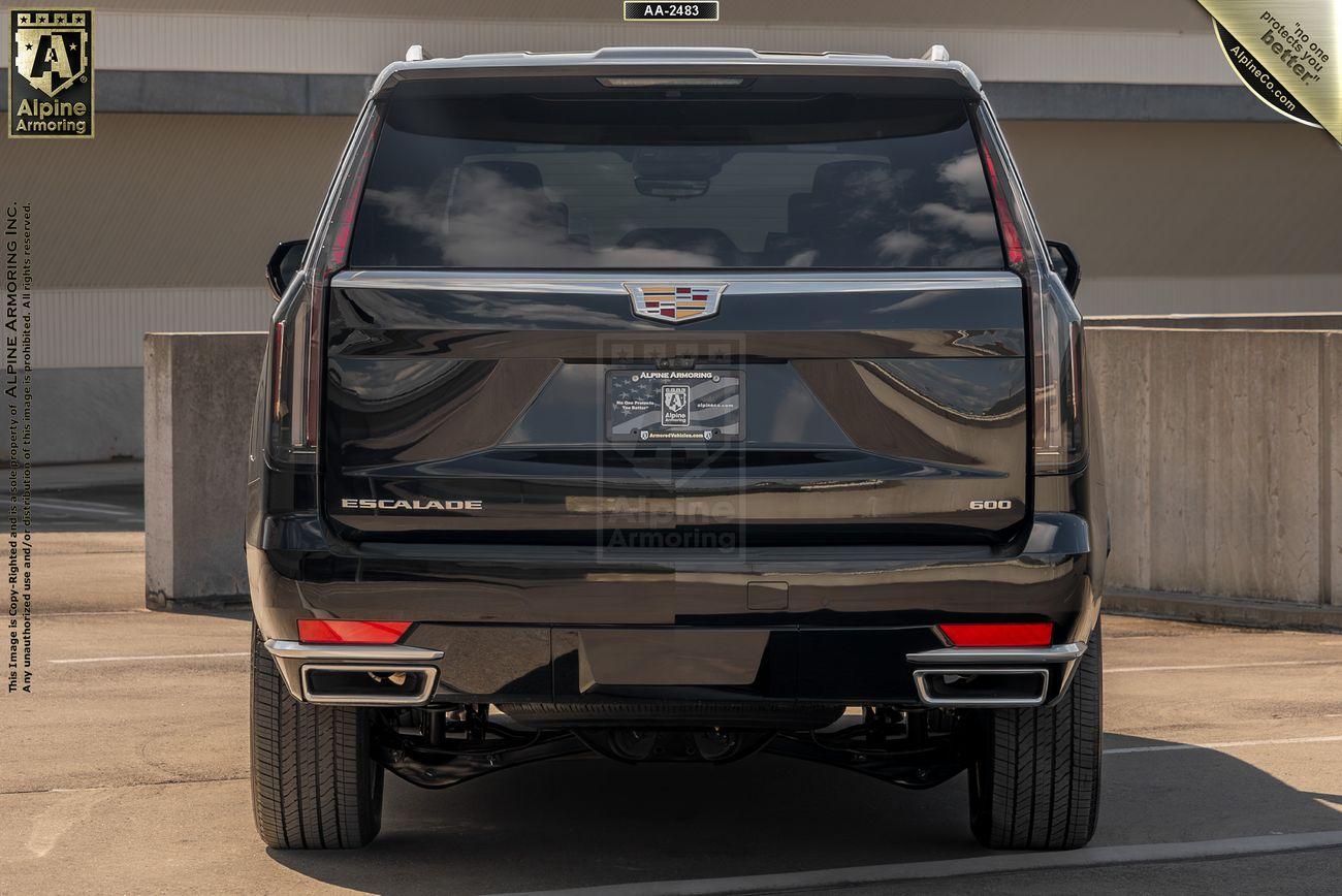 Rear view of a black  armored Cadillac Escalade ESV Premium Luxury vehicle parked in a lot, with a partially visible building in the background and a display license plate mounted on the back.