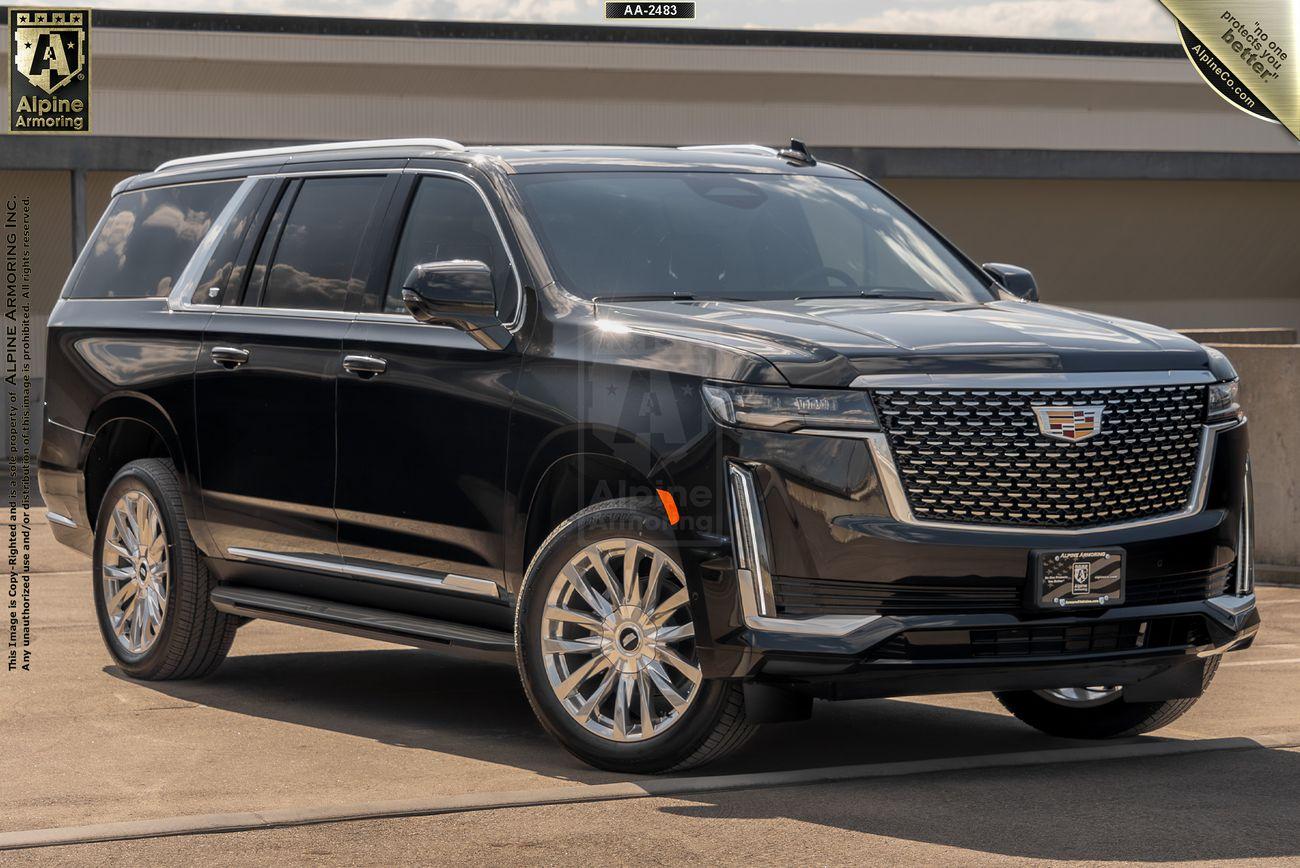 A black armored Cadillac Escalade ESV Premium Luxury SUV is parked outside on a clear day. The vehicle has a prominent grille, large wheels, and tinted windows.