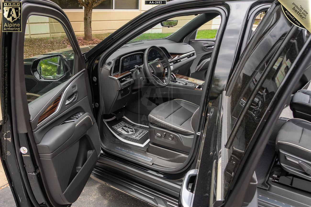 Interior view of a black  armored Cadillac Escalade ESV Premium Luxury SUV showing front and back seats, with open doors revealing a dashboard and leather upholstery.