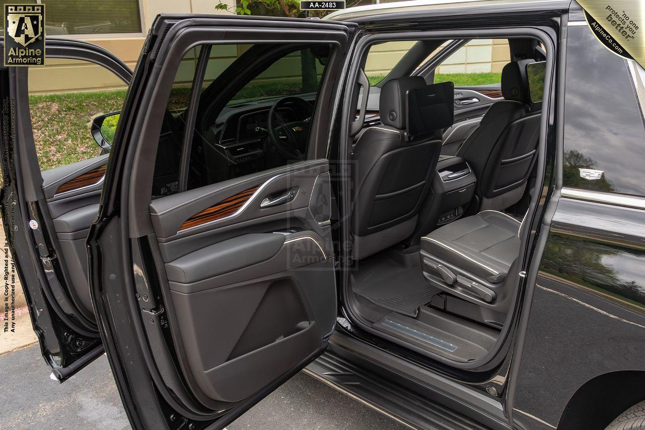 Interior view of an armored Cadillac Escalade ESV Premium Luxury SUV with doors open, showcasing leather seats, a rear entertainment system, and wood trim.