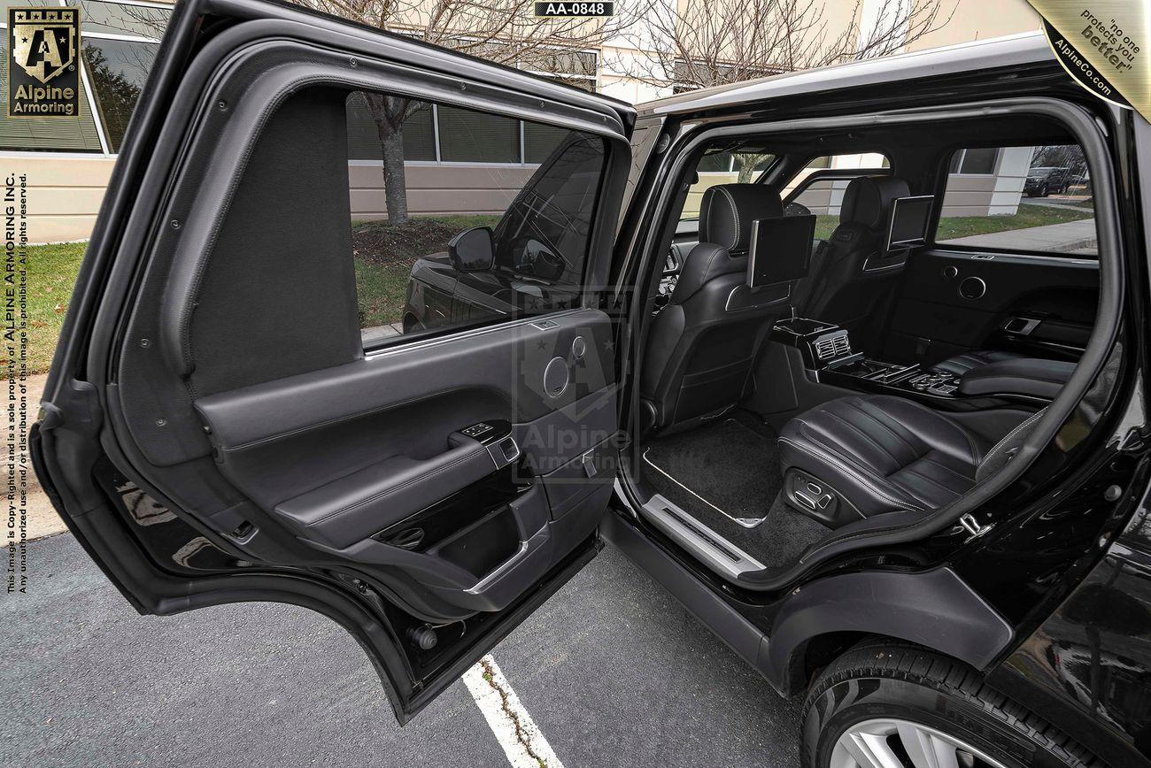 A black Range Rover Autobiography with the rear driver's door open, revealing a black leather interior and a clean dashboard. The vehicle is parked on a street beside a beige and white building.