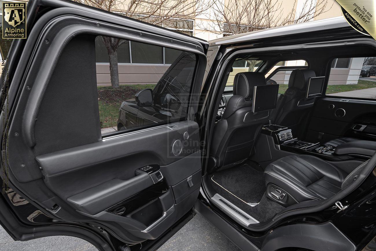 Open rear door of a black luxury armored Range Rover Autobiography showing leather seats, mounted screens, and a generously spaced interior, with part of a building visible through the window.