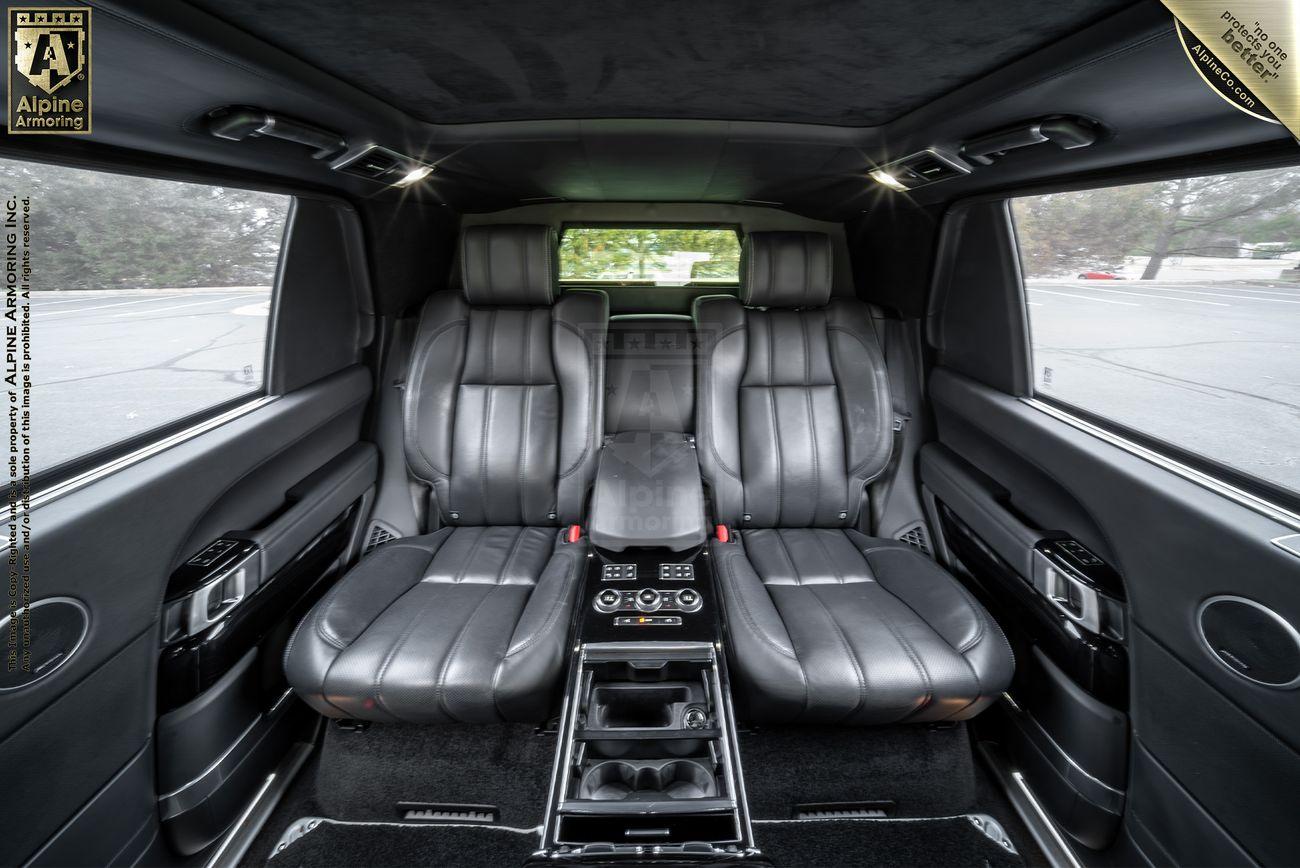 Interior of a Range Rover Autobiography SUV with leather seating, advanced control panel, and ambient lighting. An Alpine Armoring badge is visible in the upper left corner.