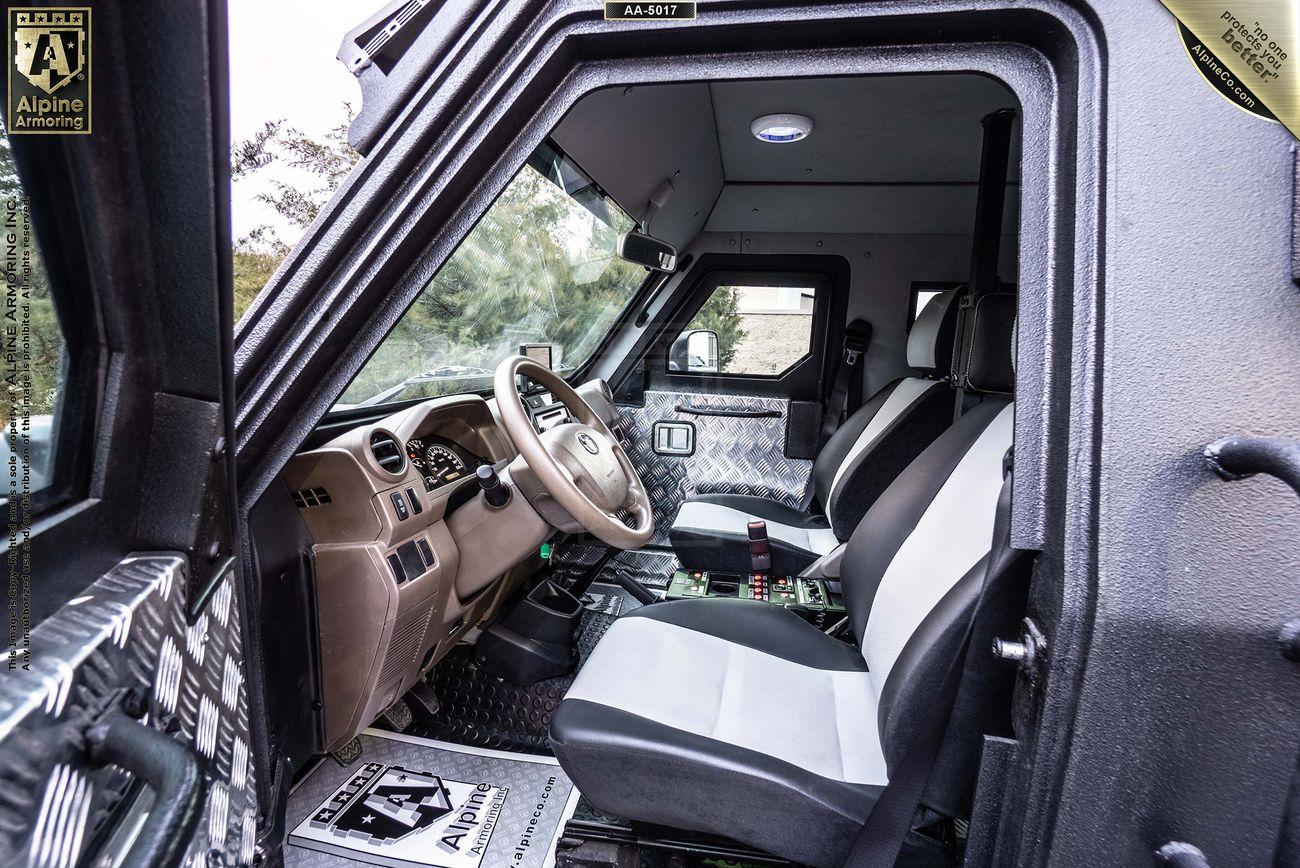 Interior view of a SWAT APC CUDA showcasing the driver's and passenger seats, steering wheel, dashboard, and door panels. The seats are black and white, and "Alpine Armoring" branding is visible.