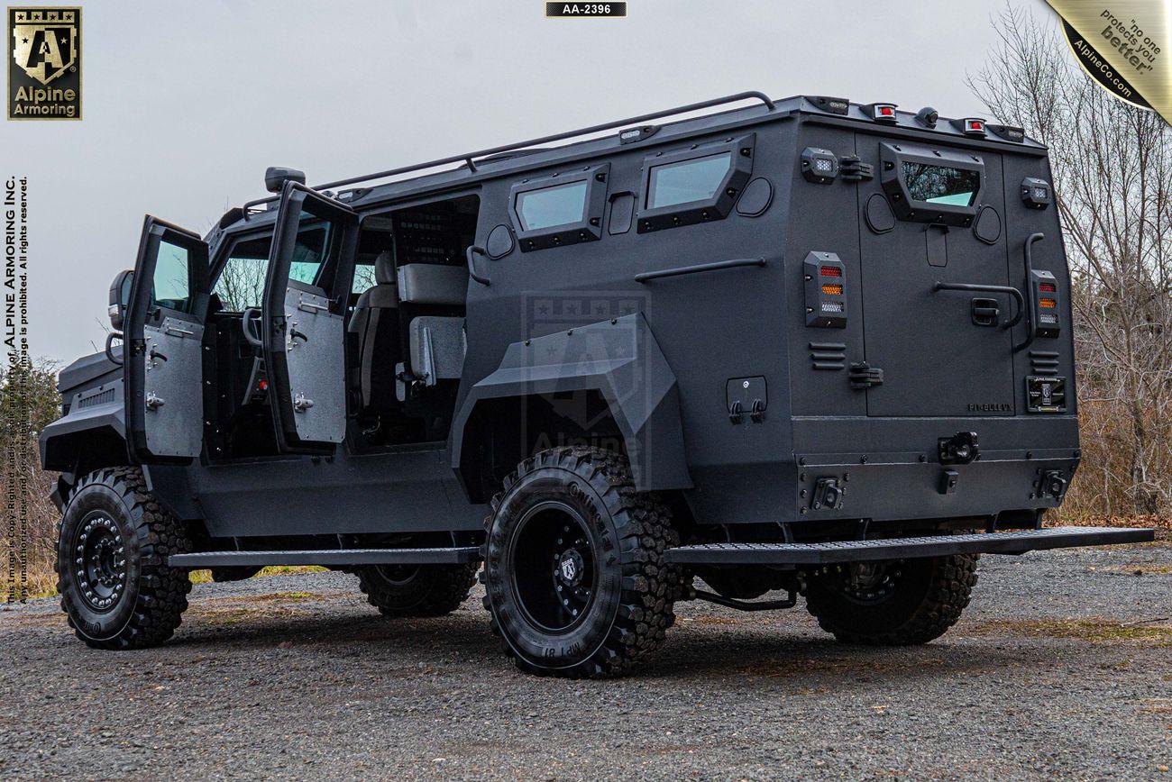 A black armored Pit-Bull VX with open side doors is parked on a gravel surface. The vehicle features large tires and multiple windows. Branding for Alpine Armoring is visible in the upper corners of the image.