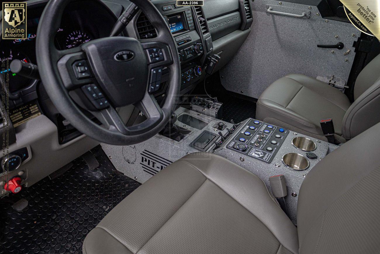 Interior of a Pit-Bull VX featuring a steering wheel, dashboard with controls, center console with multiple switches, cup holders, and front seats covered in light-colored upholstery.