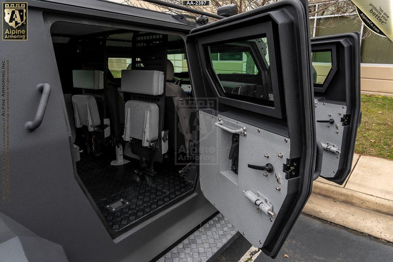 Doors of an armored black Pit-Bull VXT are open, revealing its interior with two seats and secured windows. The exterior shows a dark, matte finish.