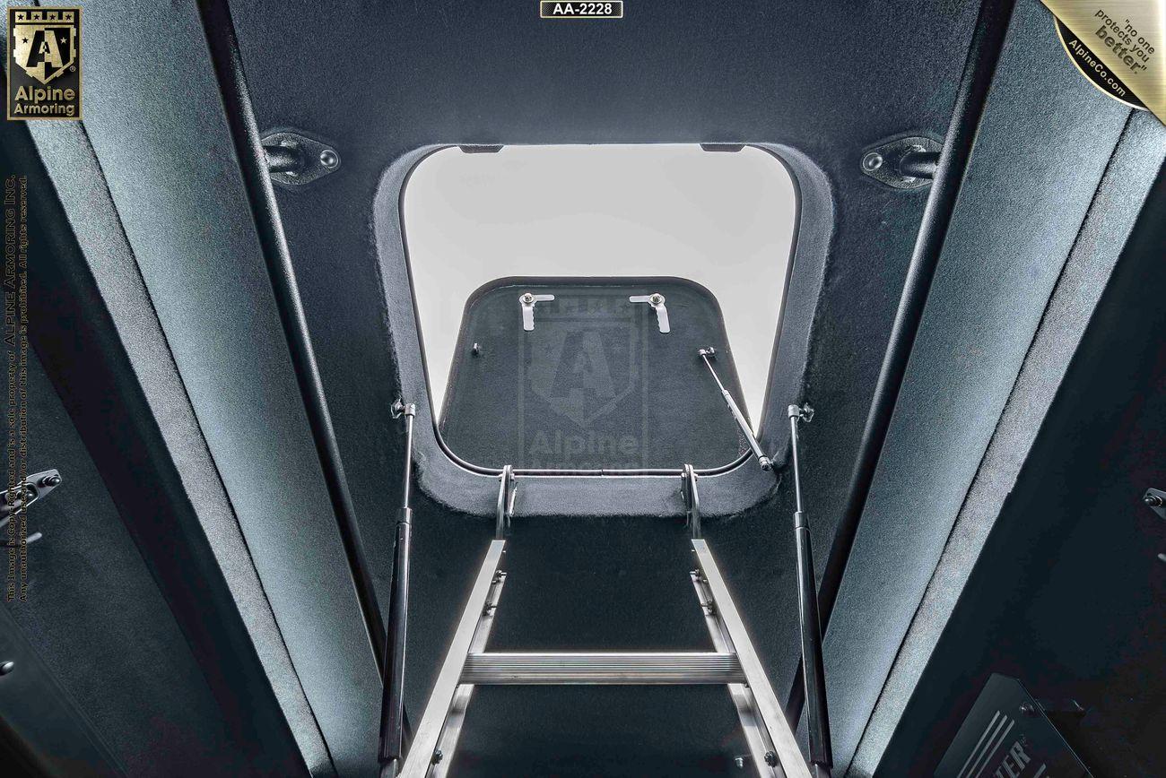 Interior view of a SWAT VAN - Pointer Based on Ford Transit showing a ladder leading to an open roof hatch surrounded by metallic surfaces with 'Alpine Armoring' logos visible on both sides.