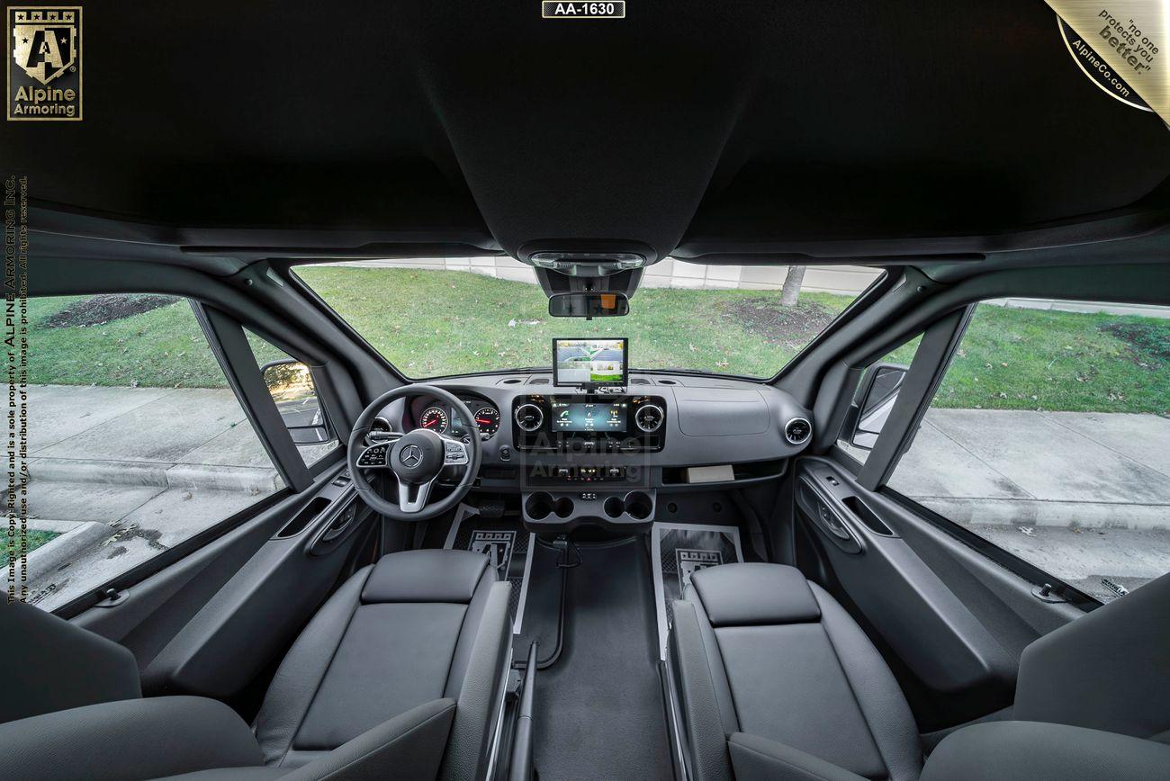 Interior view of an armored Pointer based on Mercedes Sprinter 3500XD van'scockpit, featuring two seats, a central control panel with a digital screen displaying navigation, and large windows providing a clear outside view.