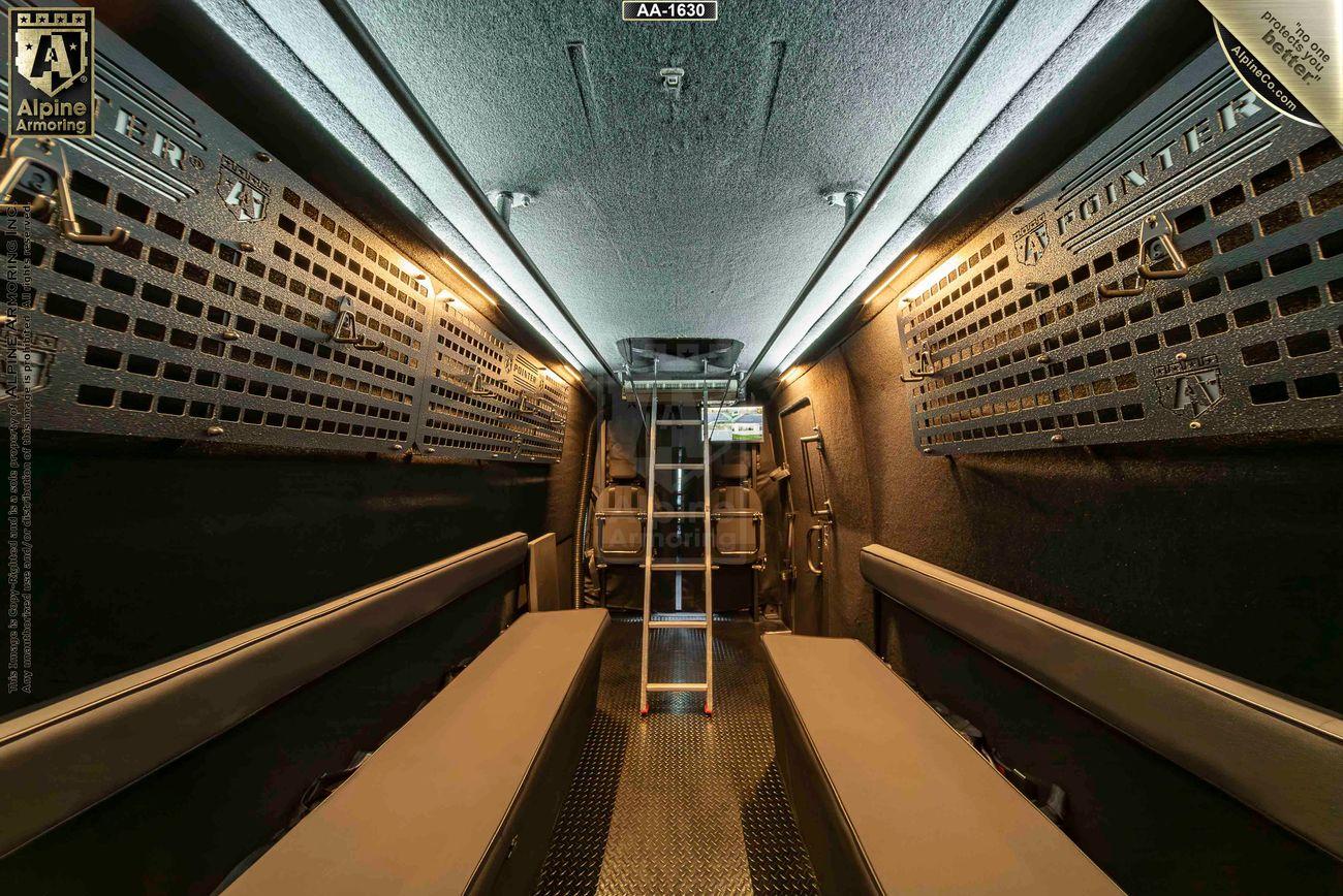 Interior view of a tactical van, a Pointer based on Mercedes Sprinter 3500XD, featuring padded benches, metal panels on the walls, and a central ladder leading to an upper compartment.