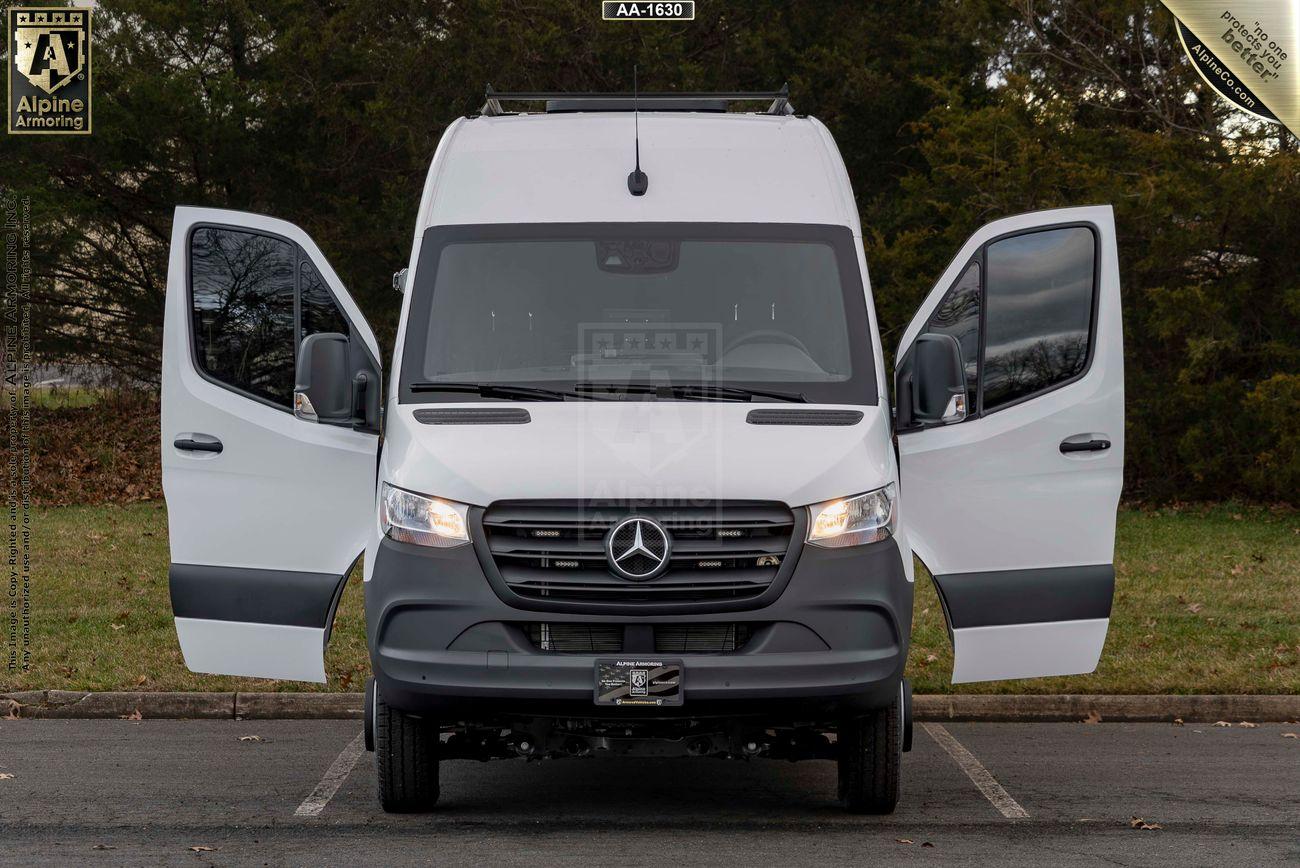 A white armored SWAT Van - Pointer® Based on Mercedes-Benz Sprinter with both front doors open, parked in an outdoor setting with trees in the background.