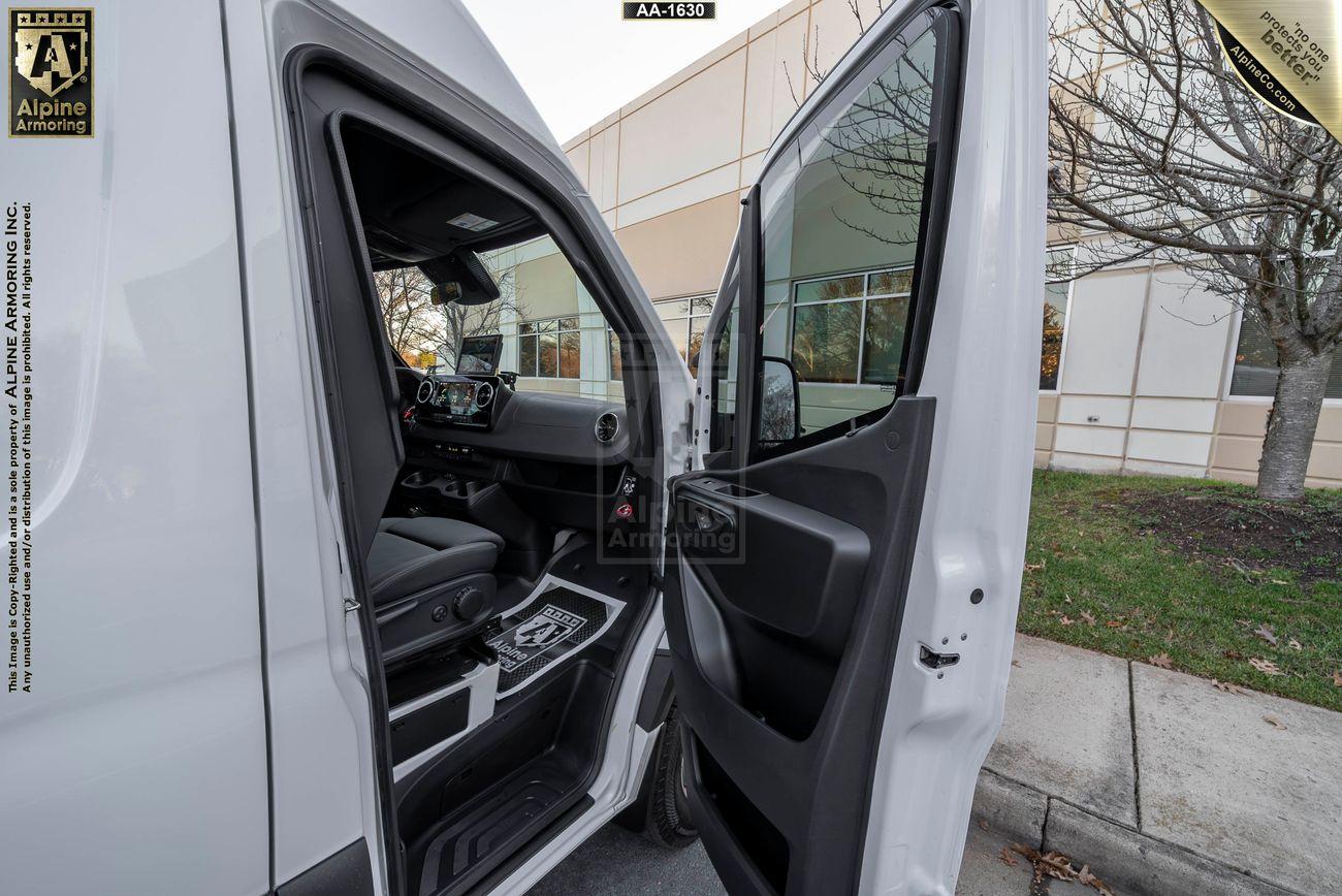 Front passenger door of a white armored Pointer van is open, revealing the interior. The background shows a sidewalk and a windowed building. 