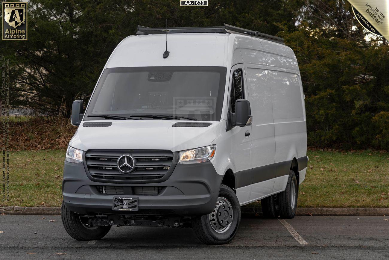 A white SWAT Van - Pointer® Based on Mercedes-Benz Sprinter  is parked on a paved area in front of greenery. The van has a black grille and front bumper and is positioned at a slight angle.