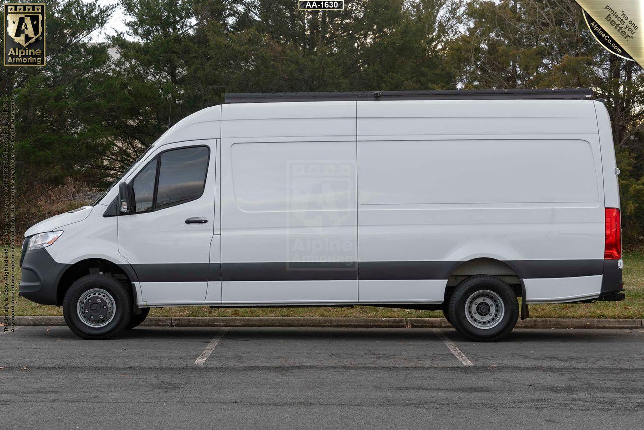 Side view of a white, high-roof armored Pointer van parked outside in a parking lot with trees in the background.