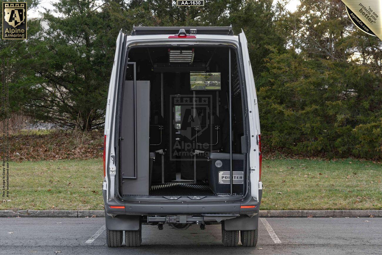 Back view of a parked white SWAT Van - Pointer® with its rear doors open, revealing a built-in cabinet and various equipment inside. Trees and grass are visible in the background.