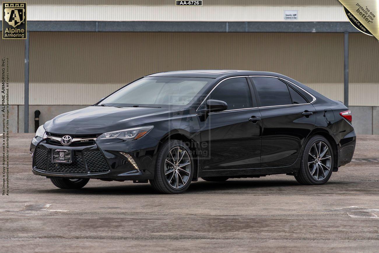 A black Toyota Camry sedan is parked on a concrete surface in front of a building. The car is viewed at an angle from the front and side.