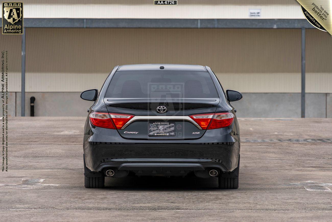 Rear view of an armored black Toyota Camry XSE parked in an empty lot with a license plate holder displaying dealership information.