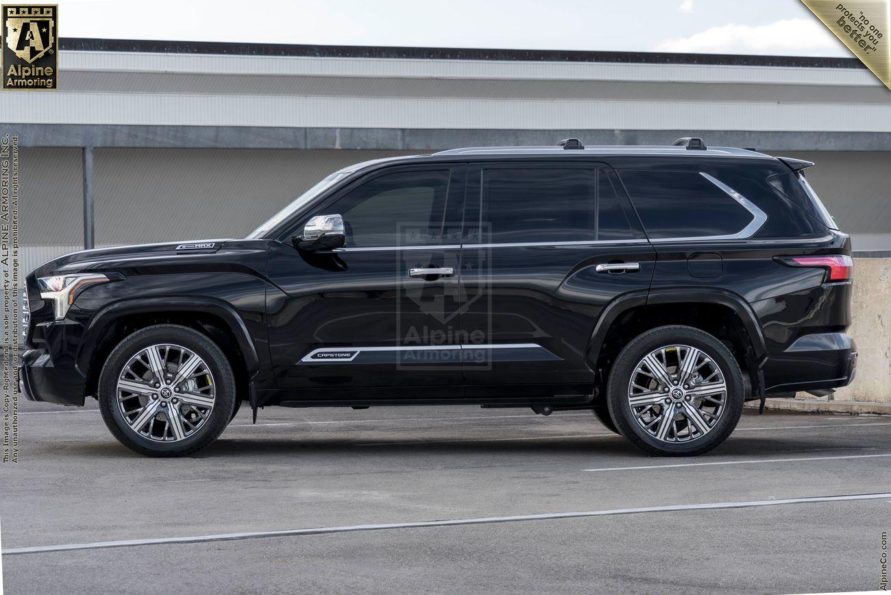 "A black armored Toyota Sequoia Capstone from Alpine Armoring, parked in an outdoor setting. The vehicle is shown in a side profile view, highlighting its sleek design, robust build, and high-end features. 