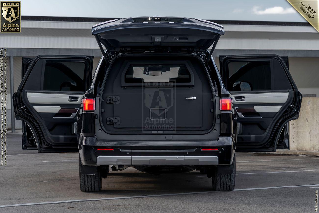  A white armored Toyota Sequoia Capstone from Alpine Armoring with two doors open  parked outdoors on a sunny day, with greenery and trees in the background.