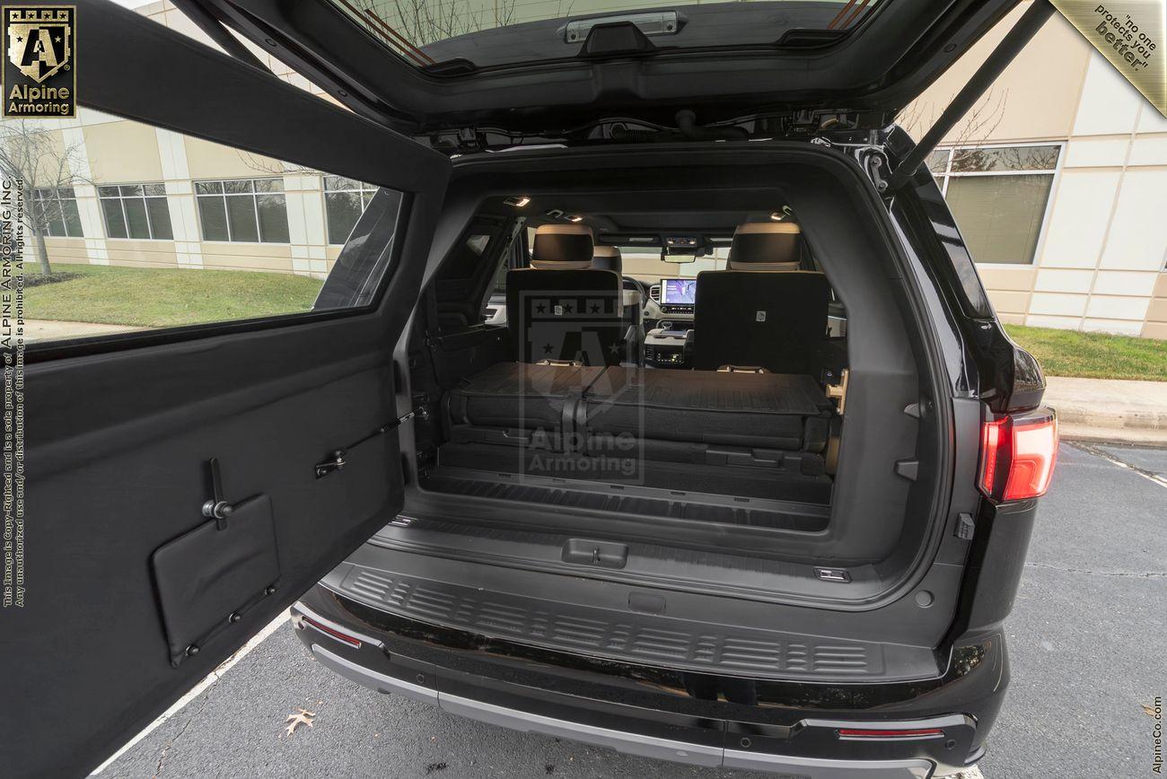 The open trunk of a black armored Toyota Sequoia Capstone from Alpine Armoring, showcasing the spacious interior with folded rear seats for additional cargo space. 