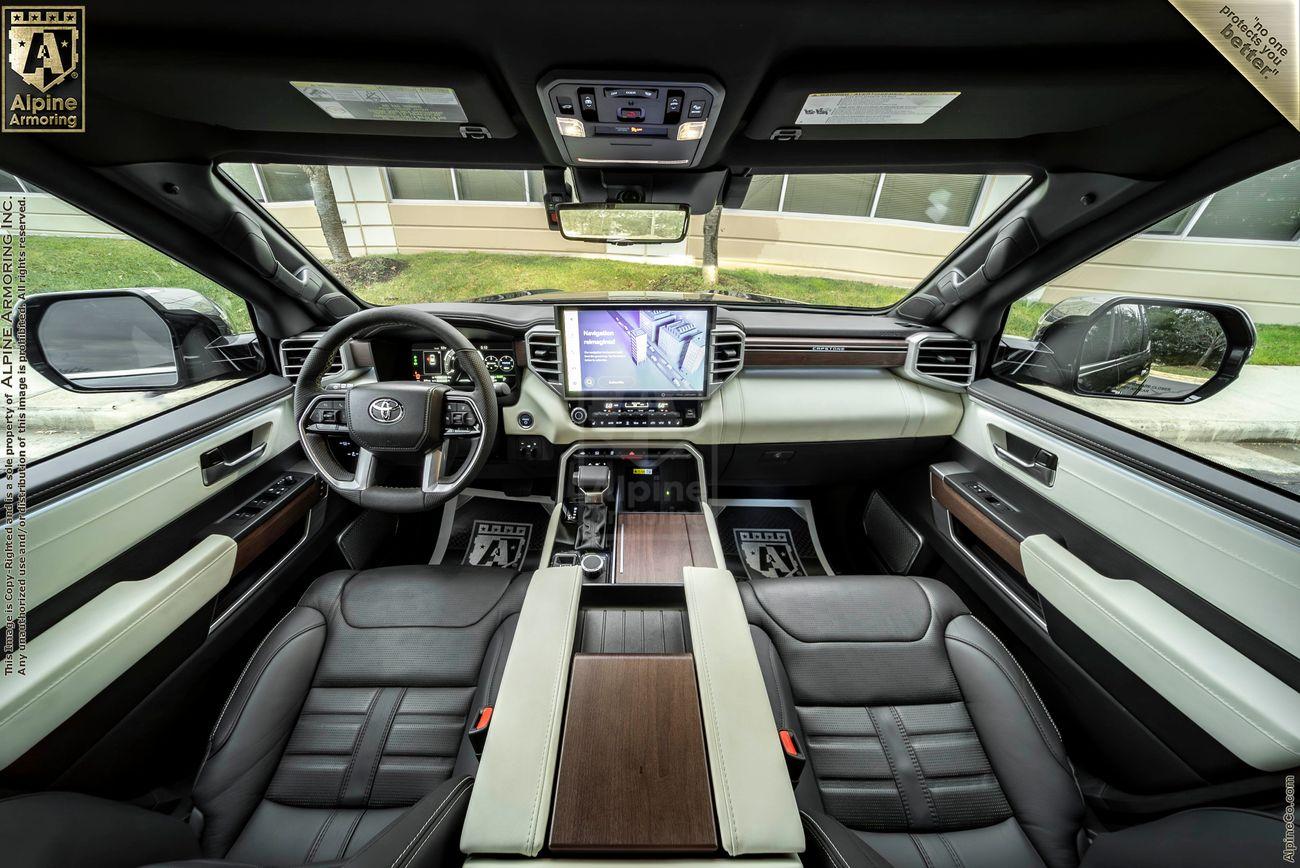 A view  of the dashboard from a white armored Toyota Sequoia Capstone from Alpine Armoring parked on a sunny day, with lush greenery and trees in the background.