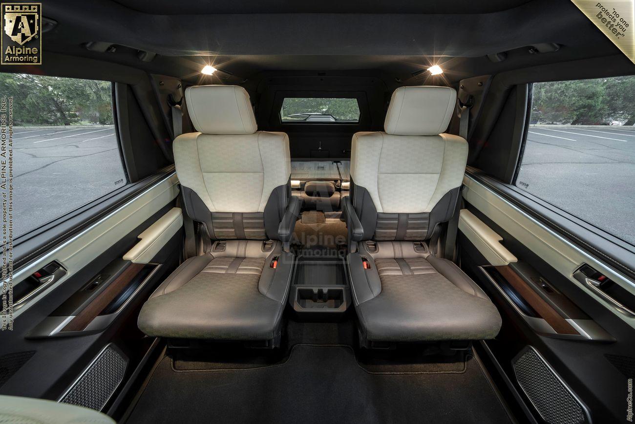 The interior of a white armored Toyota Sequoia Capstone from Alpine Armoring parked on a paved surface with greenery and trees in the background, under a clear blue sky.