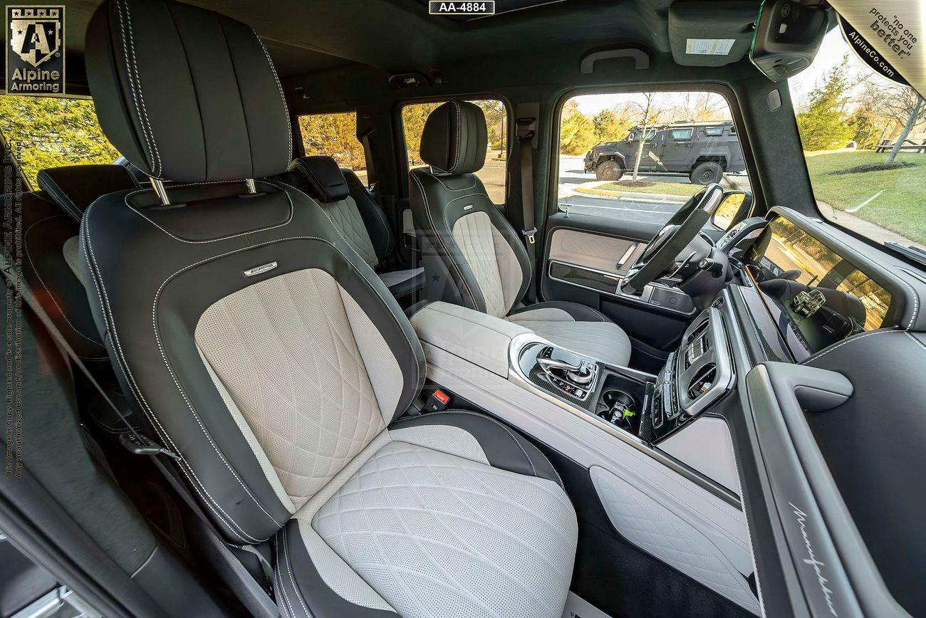 Interior of a armored Mercedes-Benz G63 AMG with quilted leather seats, a central console with controls, and large windows showing a park-like exterior.