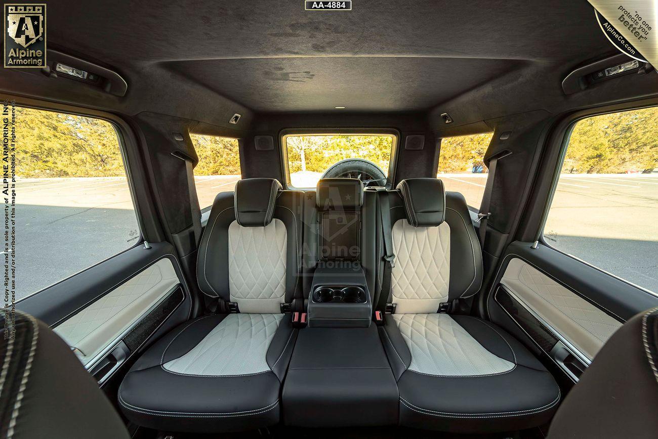 An armored Mercedes-Benz G63 AMG interior showing the back seats with a mix of black and white leather upholstery, a central console, and large windows offering a view of trees outside.