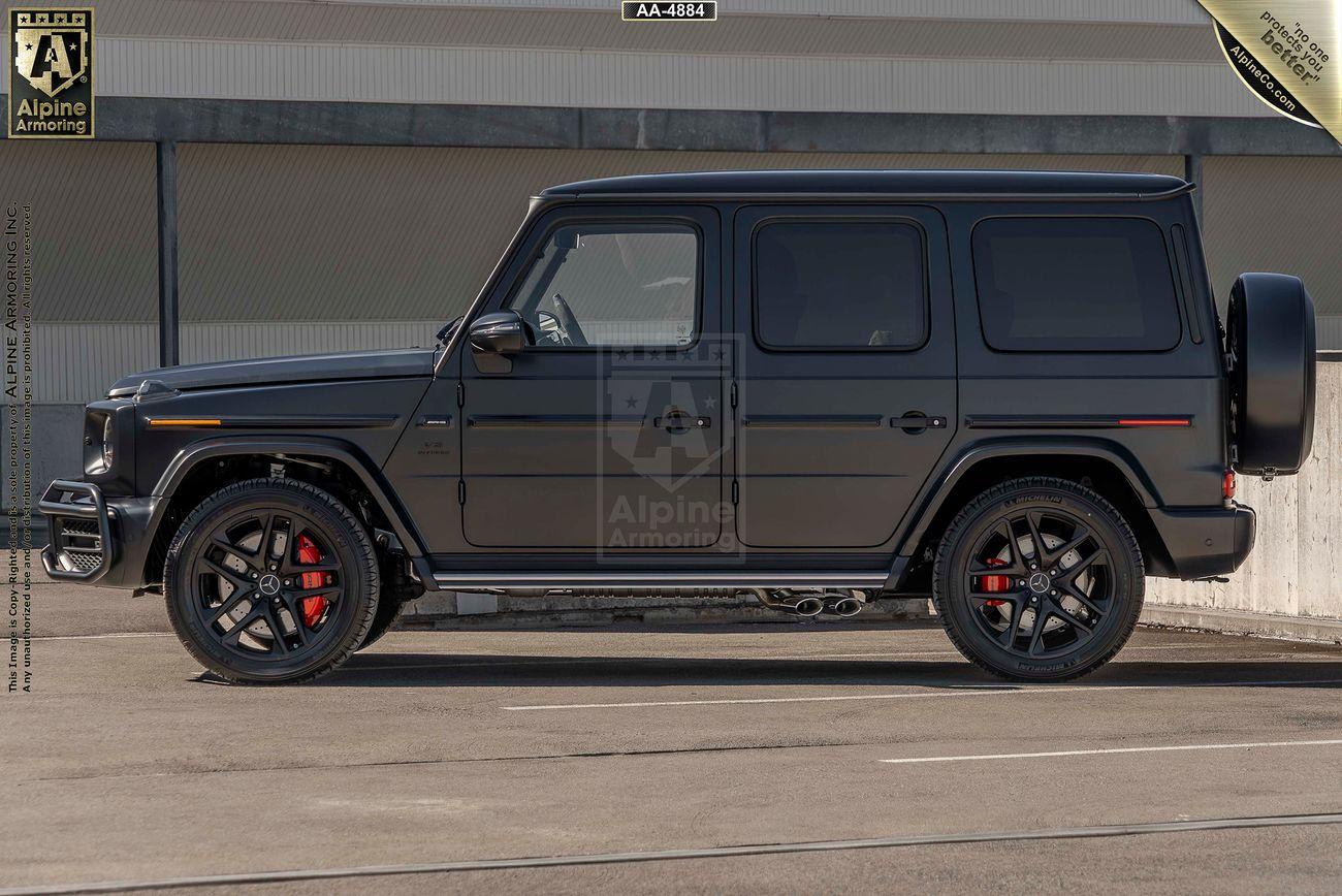 Side view of a black, armored Mercedes-Benz G63 AMG SUV parked on a paved surface, featuring red brake calipers, tinted windows, and Alpine Armoring branding.