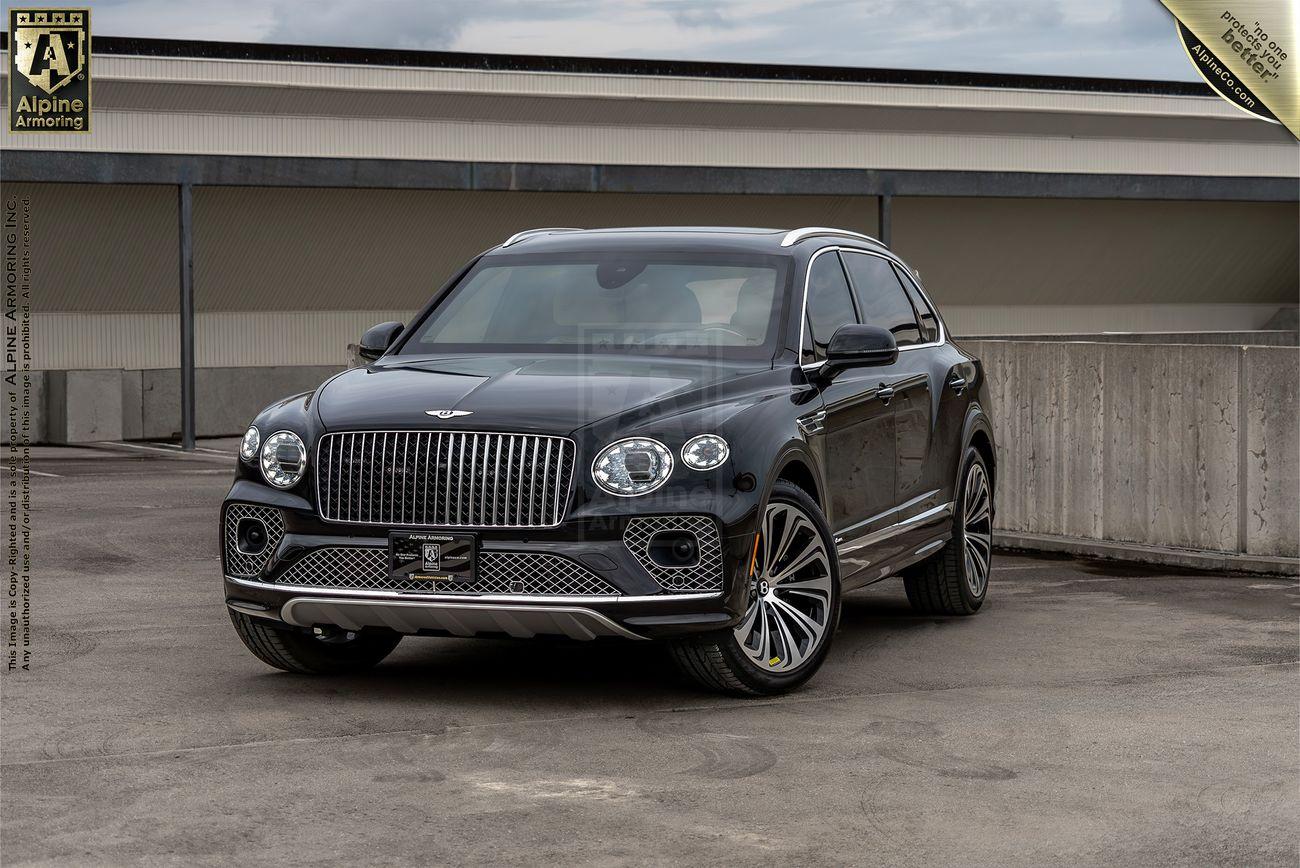 A black luxury Bentley Bentayga SUV is parked outdoors, featuring a polished exterior and alloy wheels. A building and a concrete wall are visible in the background.