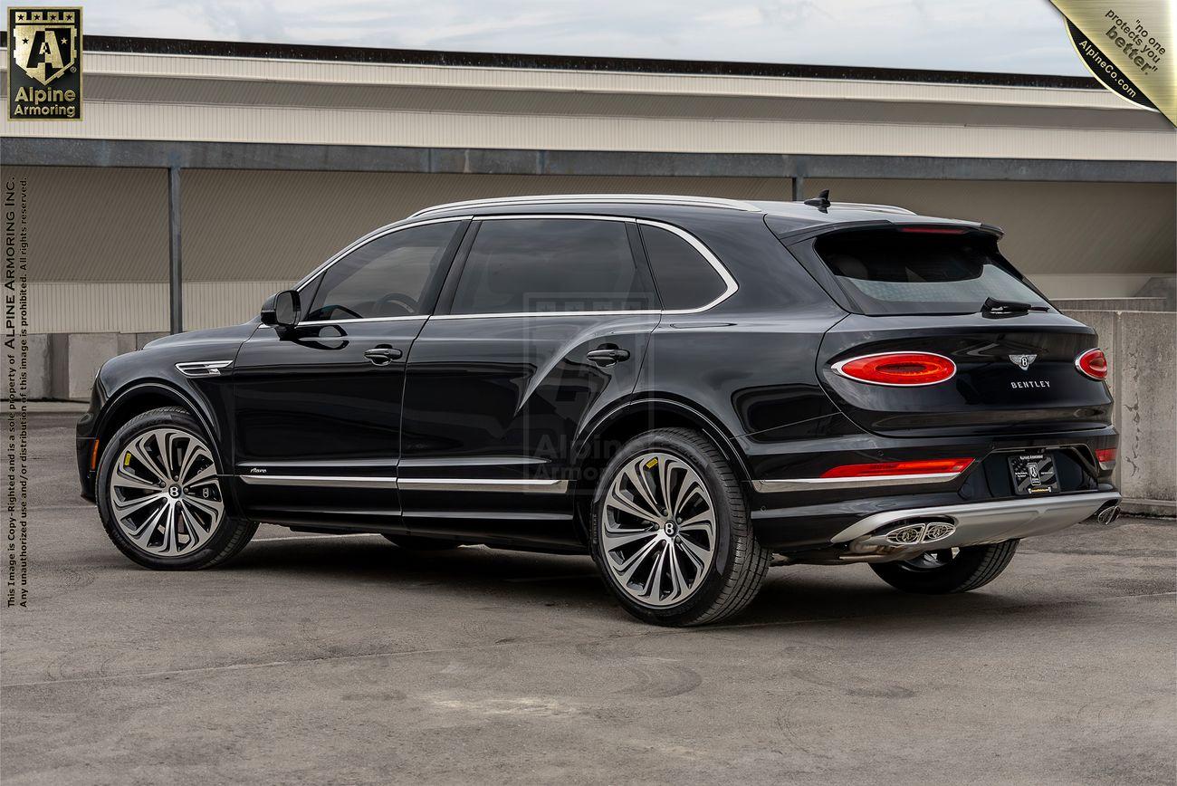 A black luxury Bentley Bentayga SUV is parked in an outdoor setting, shown from the rear side angle. The car features sleek design elements, large alloy wheels, and tinted windows.