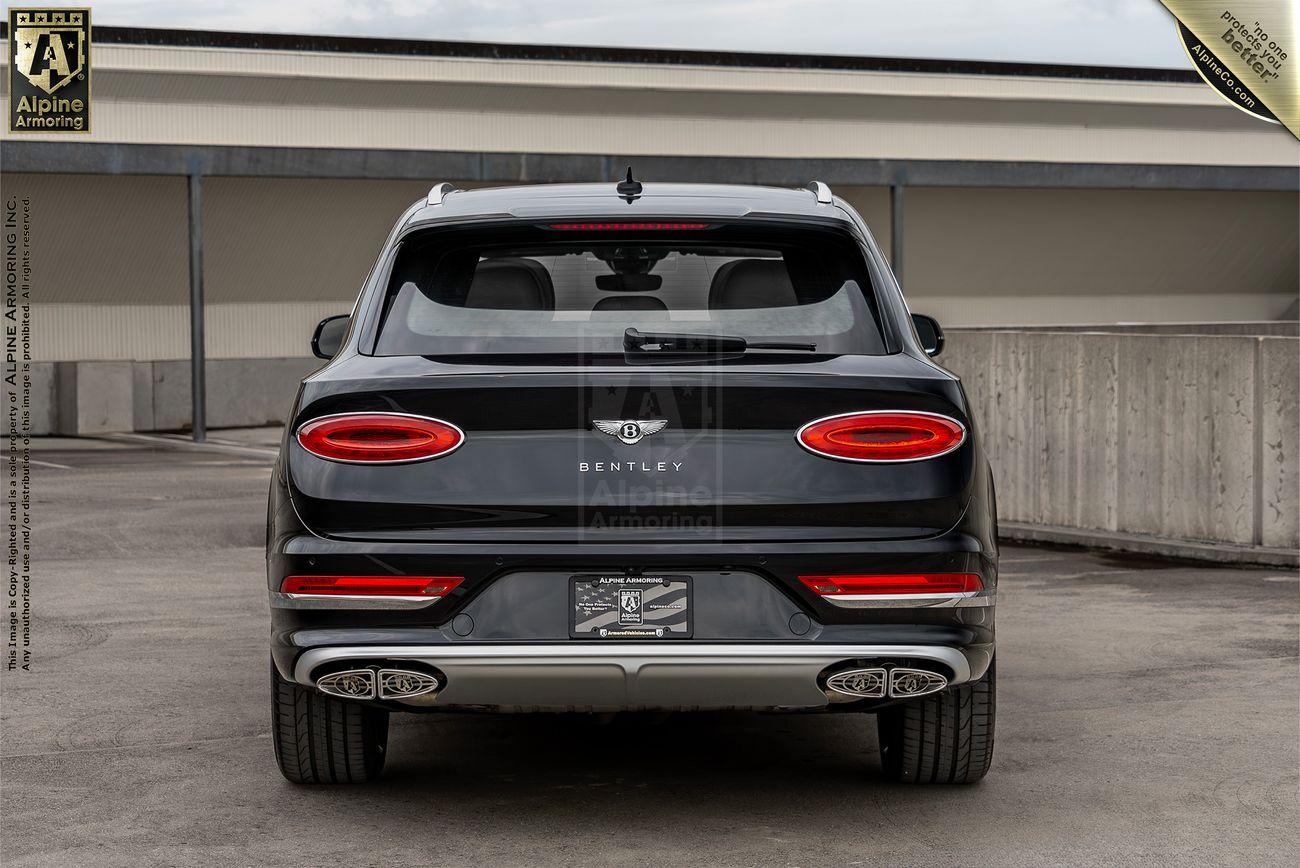 Rear view of a black bulletproof Bentley Bentayga parked in an outdoor setting, showcasing its taillights, emblem, and dual exhaust pipes.