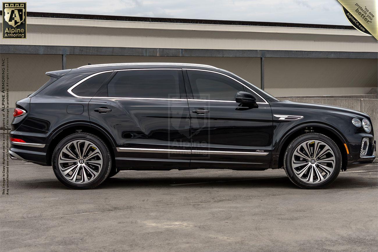 A black luxury Bentley Bentayga  SUV is parked in an outdoor setting, viewed from the side. The vehicle has large alloy wheels and sleek tinted windows.