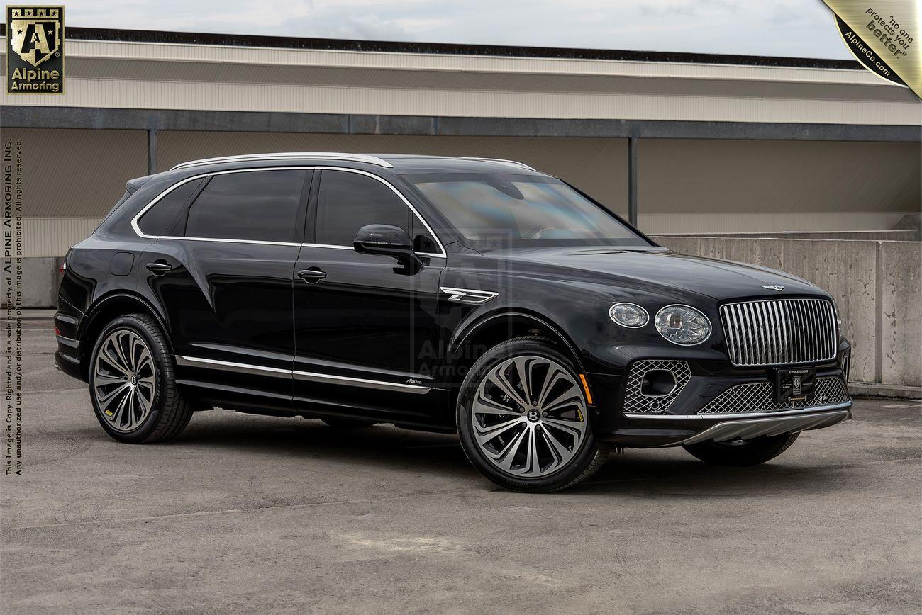 A sleek black, armored Bentley Bentayga luxury SUV is parked on a rooftop parking lot with a gray concrete wall and overcast sky in the background. The vehicle displays distinctive large wheels and chrome accents.