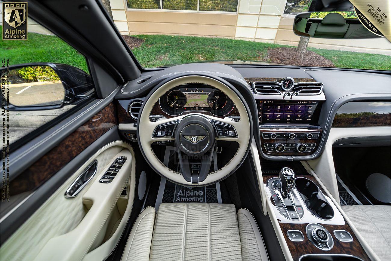 Interior view of a Bentley Bentayga 's cockpit showcasing a steering wheel, digital display dashboard, gear shift, and control panels with varied buttons and a touchscreen.