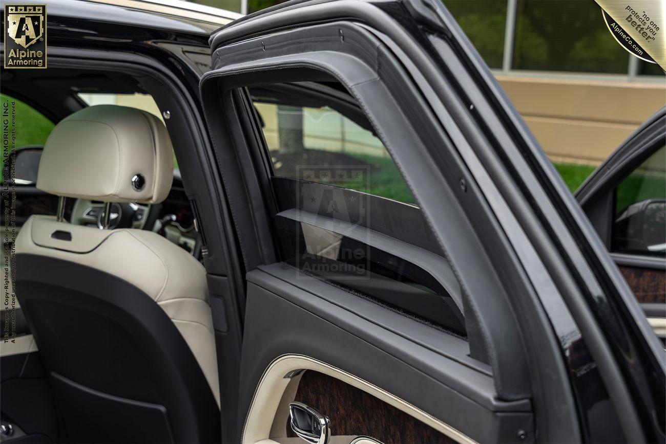 Interior of a Bentley Bentayga SUV, featuring beige leather seats and a partially open rear door, with visible wood paneling and a branded decal on the window.