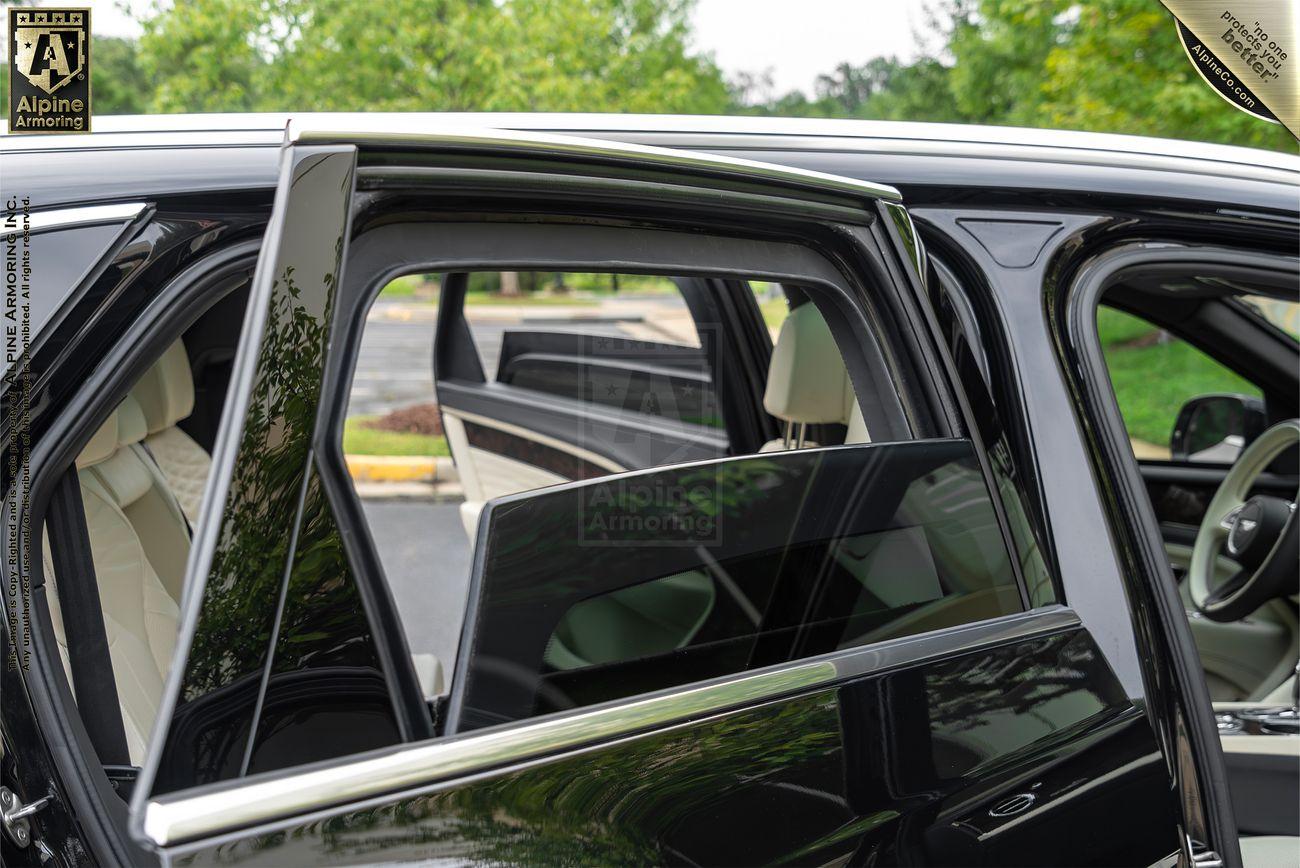 Side view of a black Bentley Bentayga SUV with all four doors open, focusing on the beige interior and the surrounding green trees in the background.