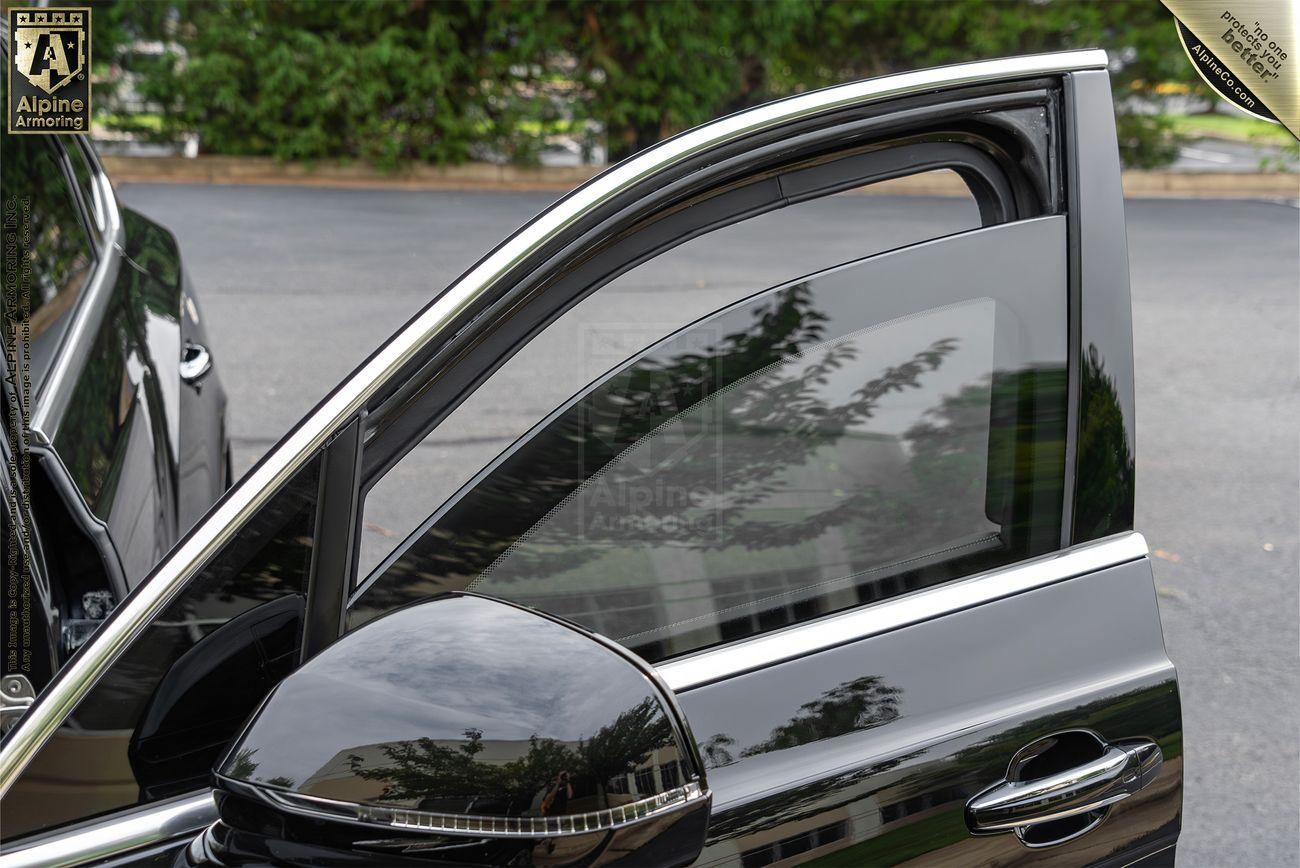 A black Bentley Bentayga with the front passenger door open and the window partially rolled down. The car is parked on a paved surface with greenery in the background.