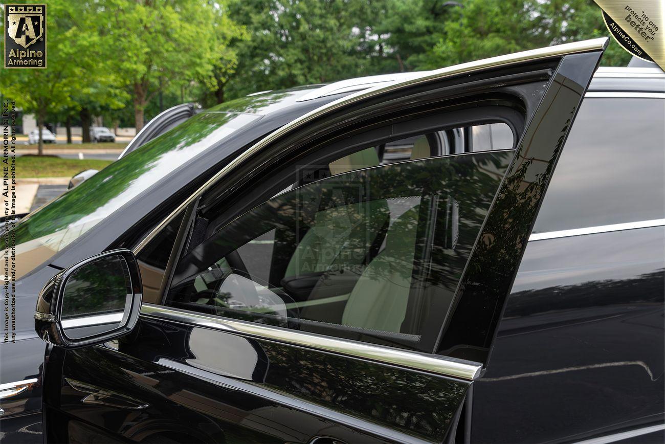 A close-up view of a black car's partly opened window with green outdoor scenery reflected on the car's surface.