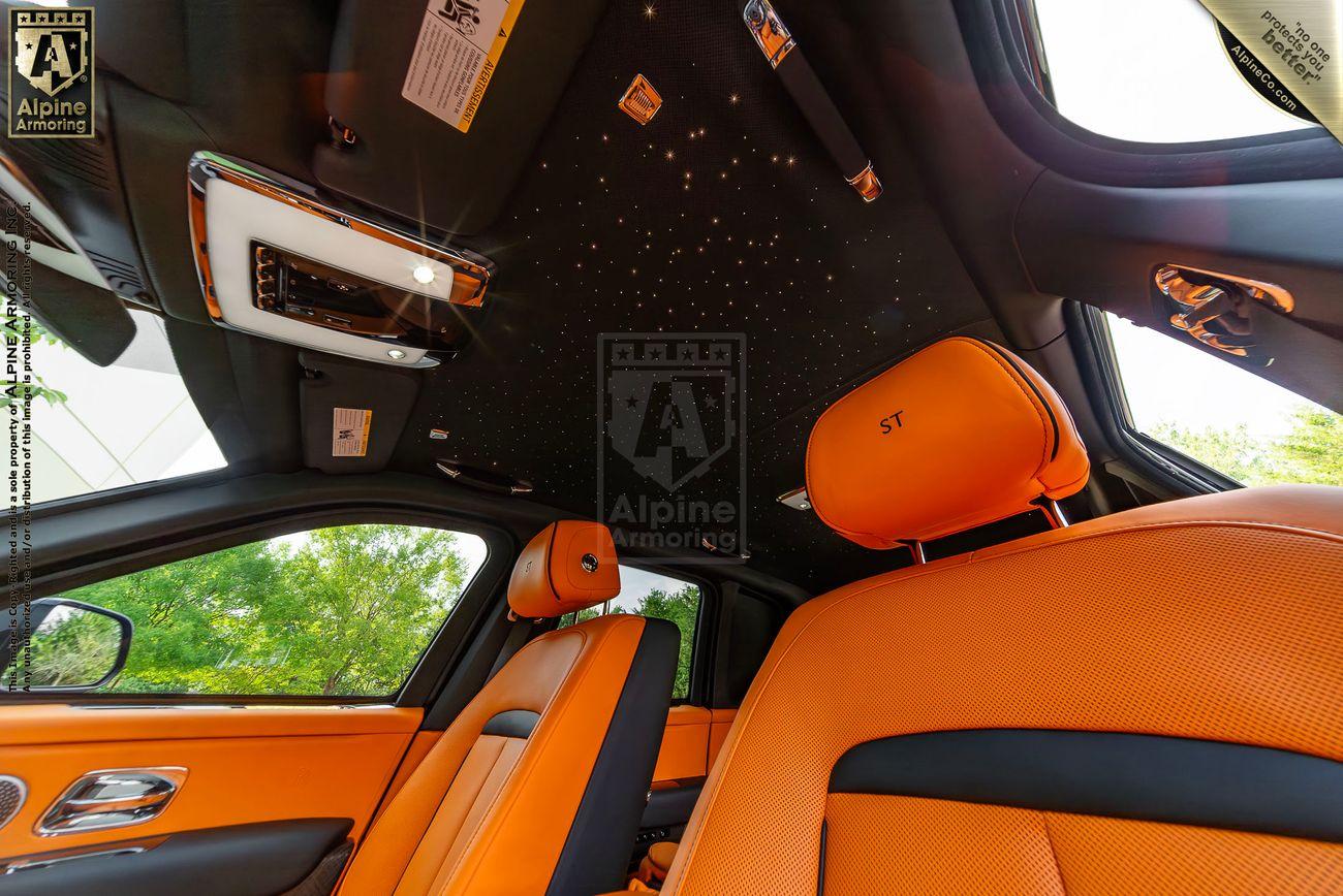 Interior view of an armored Rolls-Royce Cullinan featuring orange seats and a unique ceiling with star-like lighting.