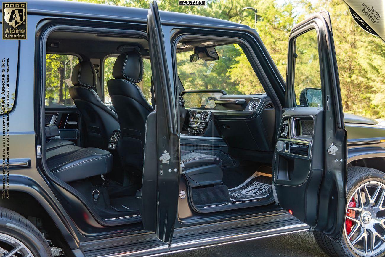 An armored  black Mercedes G63 with both front and rear passenger-side doors open, revealing the black leather interior and seating. The vehicle is parked outdoors on a sunny day.